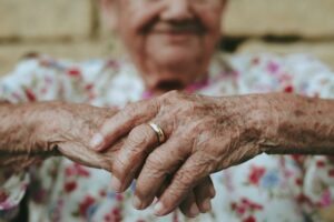 Older Woman sitting with cane, blurred in background.